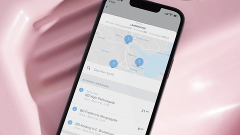 Smartphone, der viser en app til lagerstatus, placeret på en pink vask med en metalhane i baggrunden.