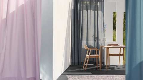 Lys og moderne indretning med farvede gardiner, et lille træbord, en stol og et spejl, der reflekterer det grønne udendørslandskab.