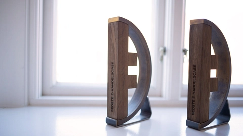 To trofæer med teksten "BEDSTE E-HANDELCASE" placeret ved et vindue, der lader lyset strømme ind.