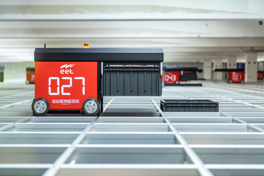 Automated storage system with large digital display showing the number 027, viewed from above in a spacious area with additional storage units visible in the background.