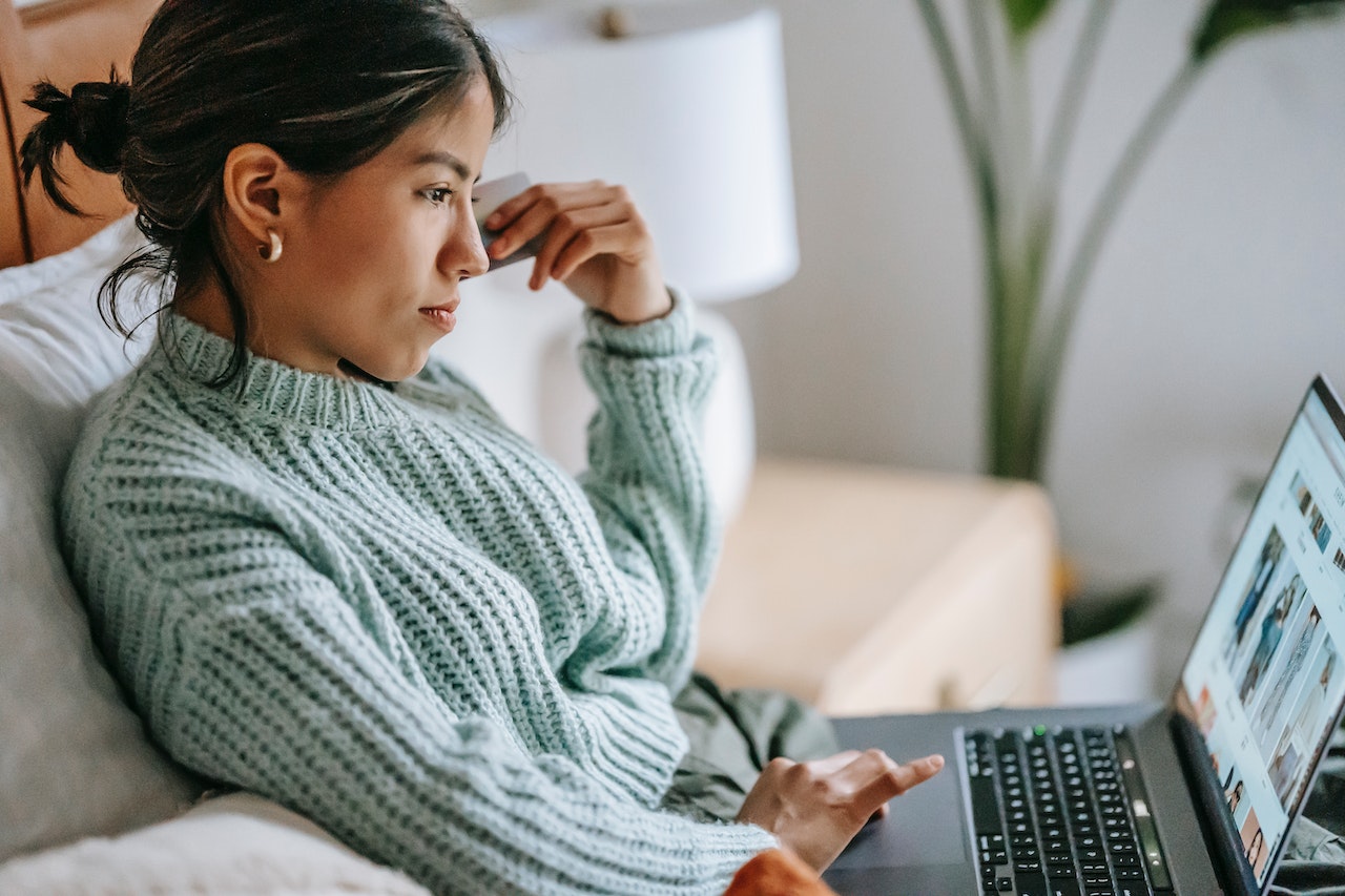 Kvinde sidder i sofa med laptop. Måske er hun frustreret over utilstrækkelig kundeservice. 