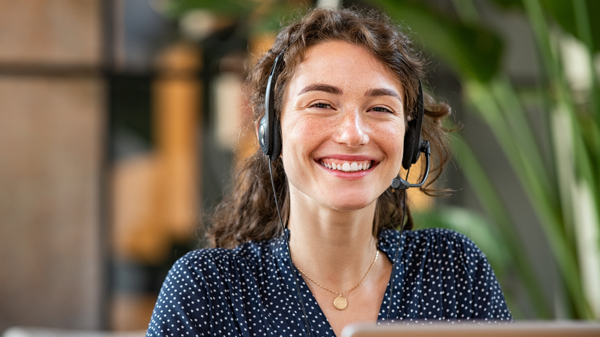 Kvinde med headset smiler til kameraet. Måske arbejder hun i en profitabel kundeservice, der er en indtægt for forretningen